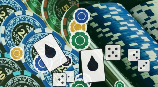 Pile of colorful casino chips with dice and a playing card hinting at gambling action on a table.